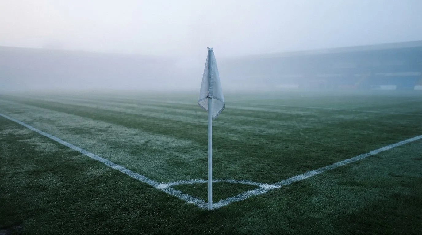 Der Rand eines Spielfelds mit weißer Linie und Eckfahne bei Nebel am frühen Morgen, ohne Menschen.