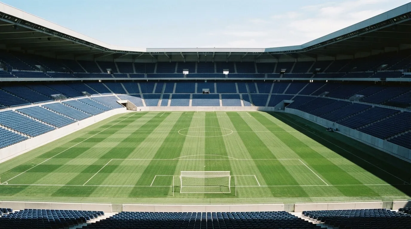 Ein leeres Fußballstadion bei Tageslicht von der Tribüne aus gesehen, der Rasen zeigt gleichmäßige Mähstreifen.