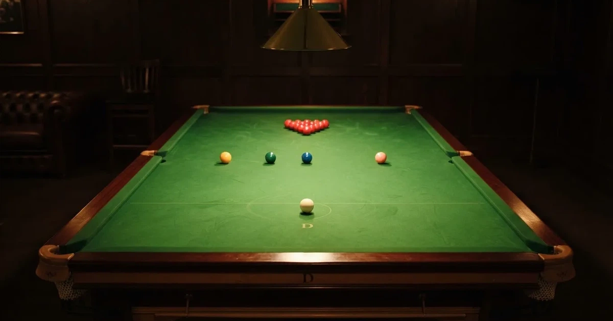 Ein Snookertisch mit grünem Tuch und aufgebauten roten Kugeln in einem abgedunkelten Raum unter einer hängenden Lampe.