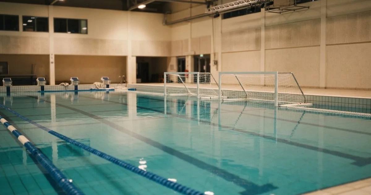 Ein Schwimmbecken mit türkisfarbenem Wasser und zwei schwimmenden Torrahmen am gegenüberliegenden Beckenrand, menschenleer unter Hallenlicht.