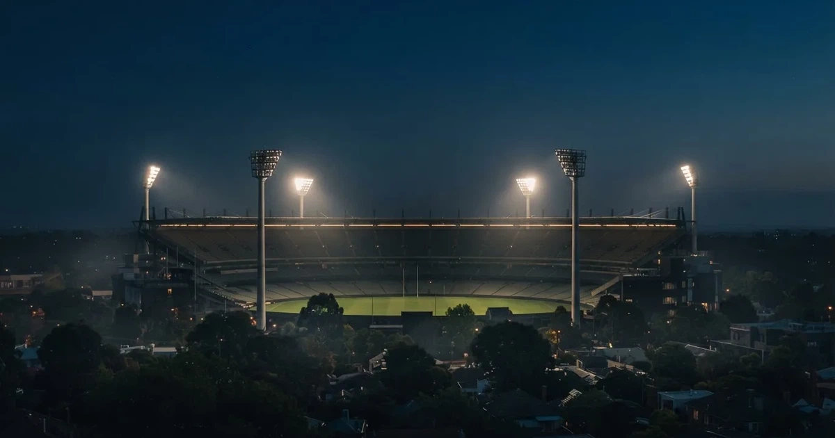 Ein Fußballstadion am Abend unter Flutlicht aus der Ferne gesehen, die Tribünen sind leicht beleuchtet und der Himmel dunkelblau.