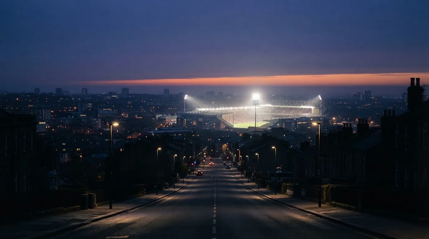 Ein Stadion unter Flutlicht aus großer Entfernung, davor eine leere Straße in der Abenddämmerung.